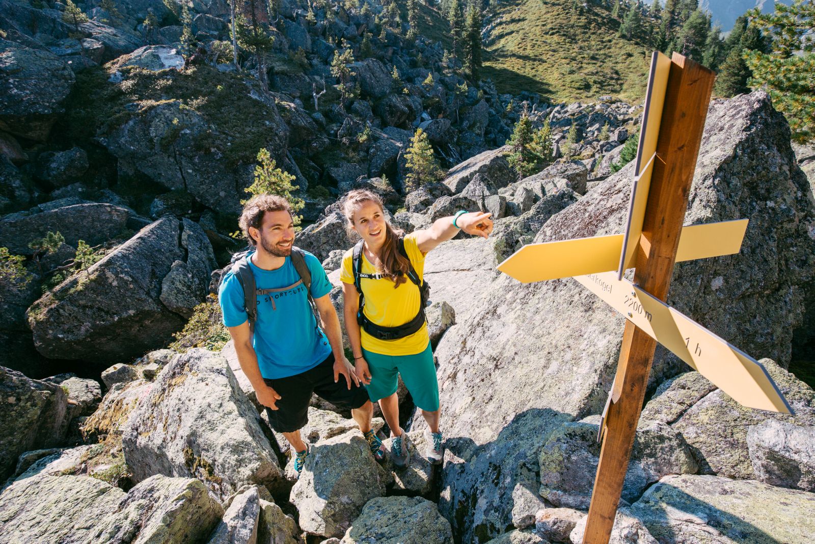 Zwei Wandernde orientieren sich an einem Wegweiser in einer felsigen Berglandschaft.
